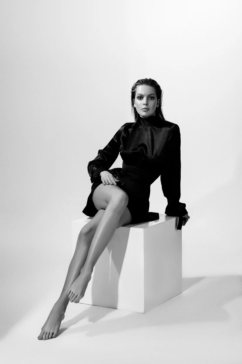 Model in einem schwarzen Kleid auf einem weißen Kubus